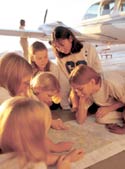 Photo of Girl Scouts studying a map in front of airplane.